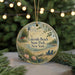 A round ornament with a lighthouse and beach scene, surrounded by greenery and a string of lights.