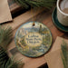 A decorative ornament featuring a scenic landscape of LaPine State Park, Oregon, with pine trees and a river, placed on a wooden surface alongside a cup of coffee and some papers.