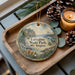 A decorative ornament featuring a scenic landscape of Larabee State Park in Washington, with pine cones, a candle, and greenery surrounding it.