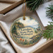 A decorative ornament with a landscape scene featuring a lake, mountains, pine trees, and a bird, hanging from a string.