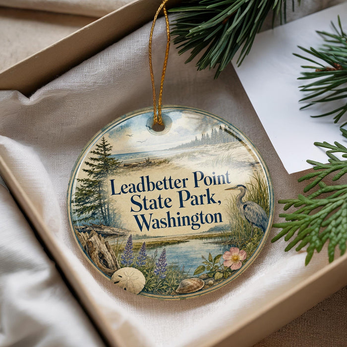 A round ornament with a scenic landscape of Leadbetter Point State Park, Washington, featuring pine trees, a lake, and a bird.