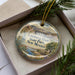 A decorative ornament with a scenic image of Leasburg Dam, a landmark in New Mexico, displayed in a box with pine branches.