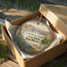 A circular ornament in a brown box, featuring an illustration of Leasburg Dam, State Park, and New Mexico.