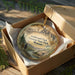 A wooden box containing a decorative ornament with a scenic landscape image and text that reads "Lewis and Clark, Caves State Park, Montana".