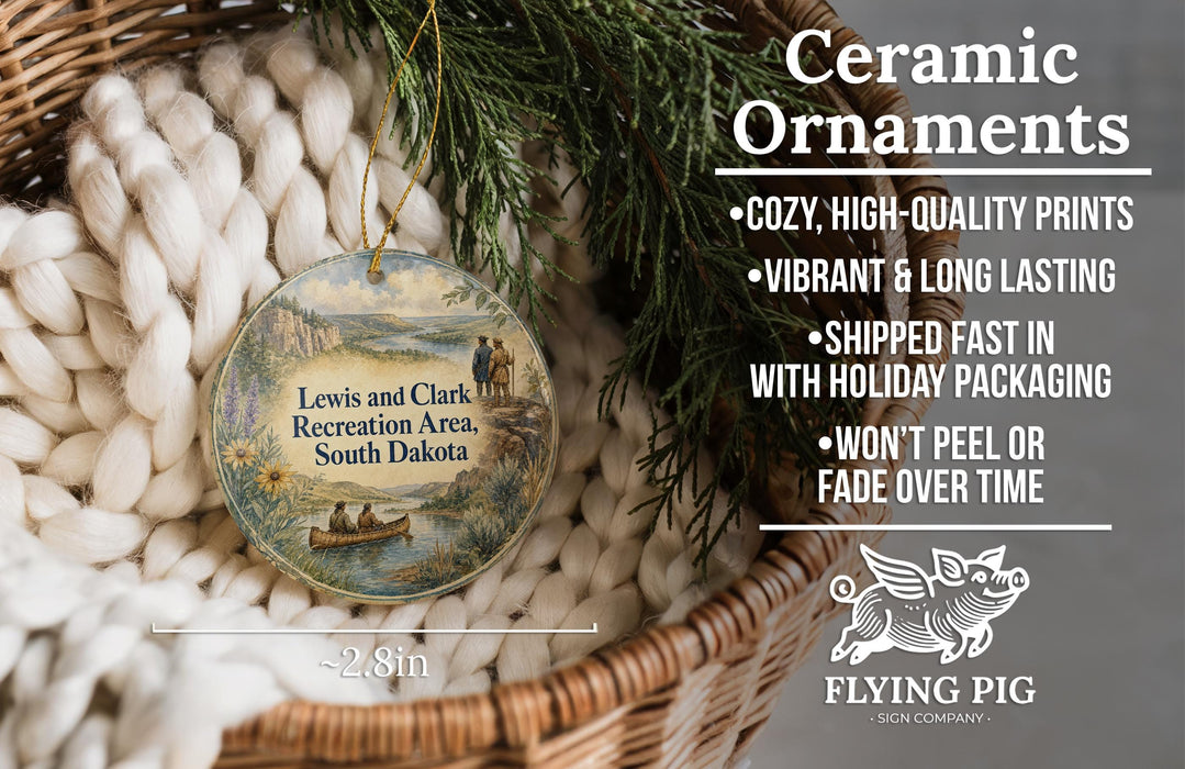 Ceramic ornaments, featuring a round ornament with a landscape scene and a bird, hanging in a basket with pine branches.