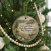 A round ornament hanging on a Christmas tree, featuring a scenic landscape with mountains, a river, and people enjoying the outdoors.