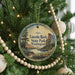 A round ornament hanging on a Christmas tree, featuring a scenic landscape with a lake and mountains.