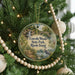 A round ornament hanging on a Christmas tree, featuring a scenic landscape with a waterfall, bridge, and birds.