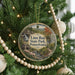 A round ornament hanging on a Christmas tree, featuring a scenic landscape with a waterfall and a bridge.