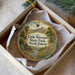 A decorative ornament in a box, featuring a scenic landscape with mountains, a river, and a cabin.