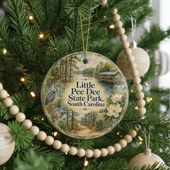 A round ornament hanging on a Christmas tree, featuring a scenic image of Little Pee Dee State Park in South Carolina.