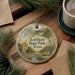 A round ornament with a scenic illustration of Lockhart State Park, Texas, is displayed on a wooden surface alongside a cup of coffee and some pine branches.