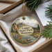 A round ornament with a scenic landscape of mountains, pine trees, and a river, hanging from a string.