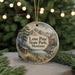 A round ornament with a painting of a cabin and mountains, surrounded by pine branches and a string of lights, representing the Lone Pine State Park in Montana.