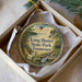 A decorative ornament in a box, featuring a scenic landscape with a river, trees, and a bridge.