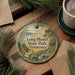 A decorative ornament with the text "Long Hunter State Park, Tennessee" on it, surrounded by pine branches and a cup of coffee on a wooden surface.