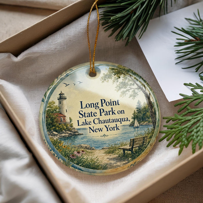 A decorative ornament with a lighthouse and a bench, surrounded by greenery, is displayed in a box.