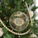 A round ornament hanging on a Christmas tree, featuring a scenic landscape with a pond, a building, and trees.