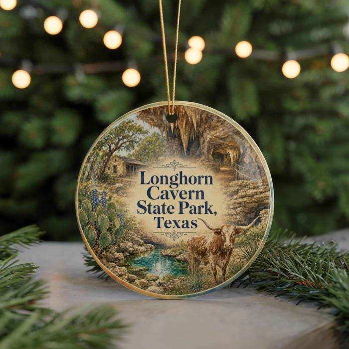 A circular ornament with a painting of a scenic landscape, featuring a cow, trees, and a pond, hanging in front of a Christmas tree with lights.
