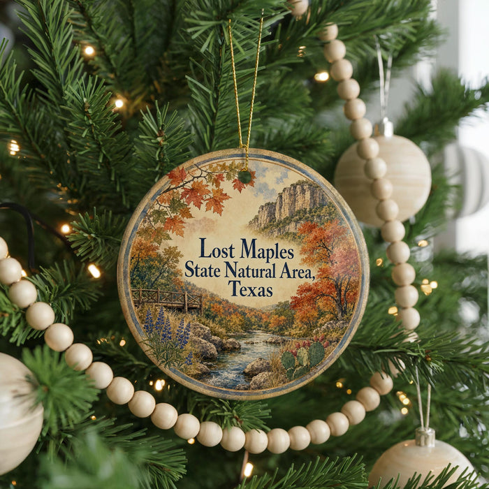 A circular ornament hanging on a Christmas tree, featuring a scenic landscape with a river, mountains, and fall foliage.