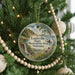 A round ornament hanging on a Christmas tree, featuring a scenic landscape of a lake, mountains, and a waterfall.
