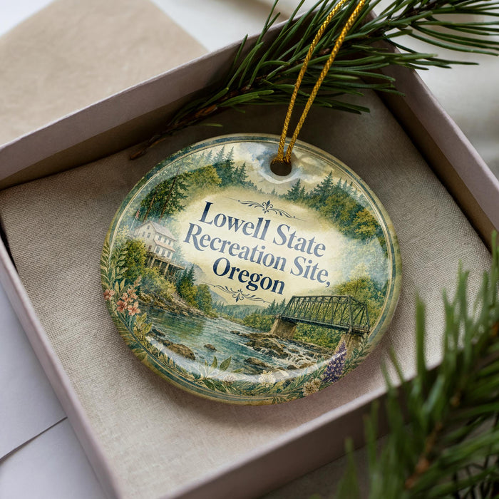A decorative ornament in a box, featuring a scenic landscape with a river, bridge, and trees.
