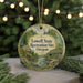 A round ornament with a scenic landscape featuring a river, bridge, and trees, hanging from a string.