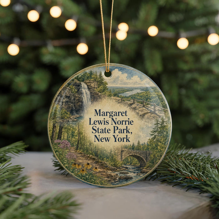 A round ornament featuring a scenic landscape with a waterfall, trees, and a bridge, hanging in front of a Christmas tree with lights.