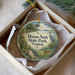 A decorative ornament in a box, featuring a scenic landscape with a bird, a bridge, and a body of water.