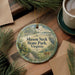 A decorative ornament with the text "Mason Neck State Park, Virginia" is displayed on a wooden surface, surrounded by pine branches and a cup of coffee.