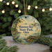 A circular ornament with a painting of a serene lake, a lighthouse, and birds in flight, surrounded by greenery and a string of lights.