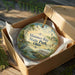 A decorative ornament in a box, featuring a scenic image of Maumee Bay State Park, Ohio.