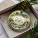 A decorative ornament in a box, featuring a scenic image of the Mayo River State Park in North Carolina.