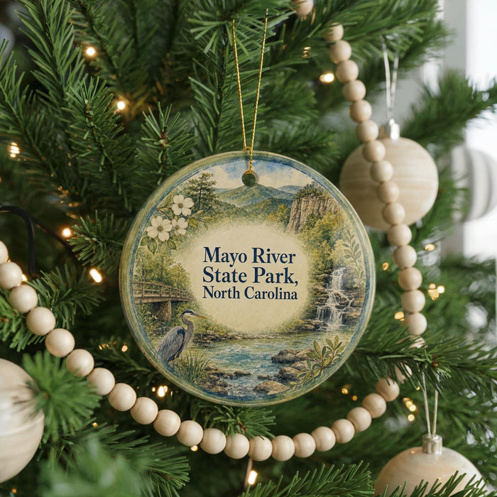 A round ornament hanging on a Christmas tree, featuring a scenic image of the Mayo River State Park in North Carolina.