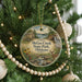 A round ornament hanging on a Christmas tree, featuring a scenic image of a park with a stream and a cabin.