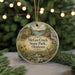 A round ornament with a scenic image of a park, featuring a deer, a waterfall, and a cabin, is displayed in front of a blurred background with Christmas lights.