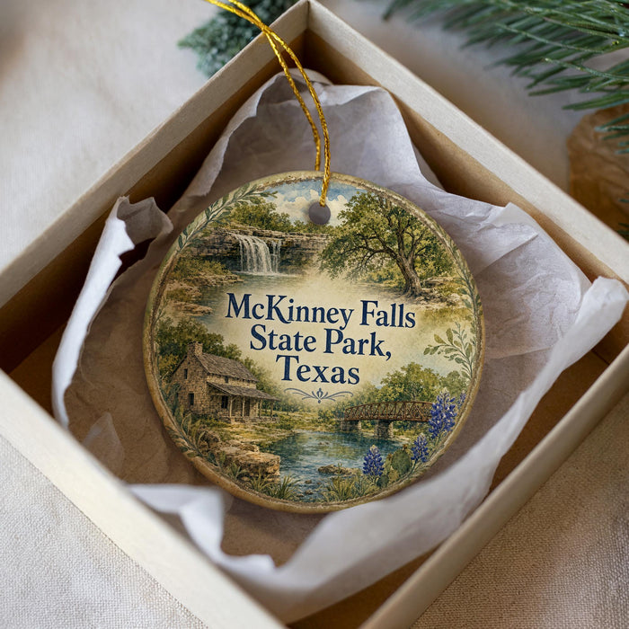 A circular ornament with a painting of a scenic landscape, featuring a waterfall and a bridge, is displayed in a box.
