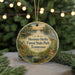 A round ornament with a painting of a forest scene hangs in front of a Christmas tree with lights.