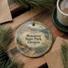 A decorative ornament with the text "MEMALOOSE STATE PARK, OREGON" is displayed on a wooden surface, surrounded by pine branches and a cup of coffee.