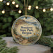 A decorative ornament featuring a scenic landscape with mountains, trees, and a body of water, hanging from a string.