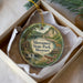 A decorative ornament in a box, featuring a scenic landscape with a river, waterfall, and a cabin, along with the text "Mermac State Park, Missouri".