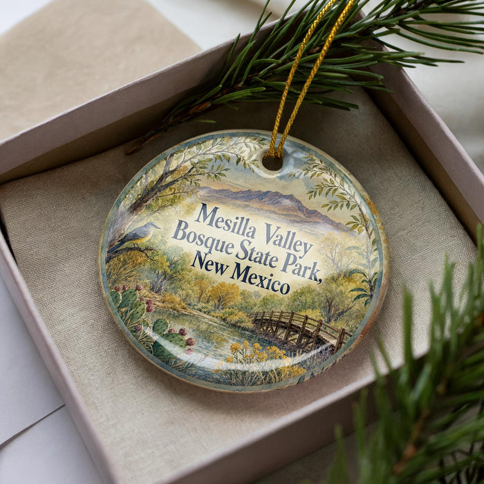 A decorative ornament in a box, featuring a scenic landscape with a bridge and mountains in the background.