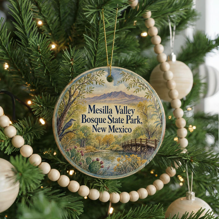 A round ornament hanging on a Christmas tree, featuring a scenic landscape with mountains, trees, and a bridge.