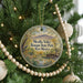 A round ornament hanging on a Christmas tree, featuring a scenic landscape with mountains, trees, and a bridge.
