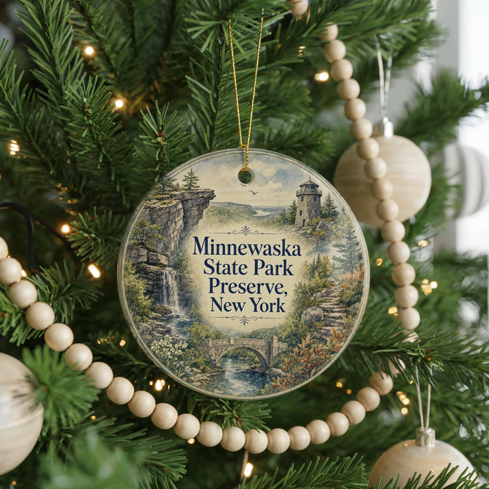 A round ornament hanging on a Christmas tree, featuring a scenic landscape with a castle, trees, and a waterfall.