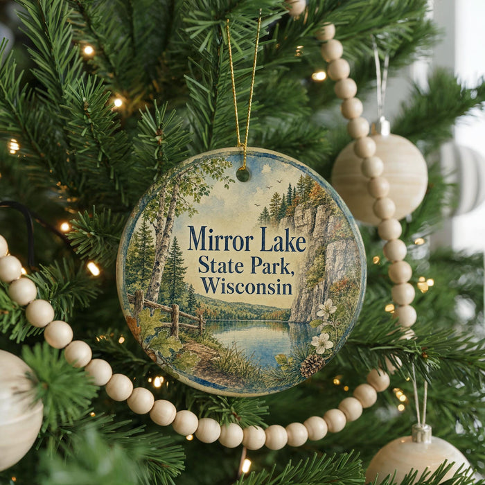 A round ornament hanging on a Christmas tree, featuring a scenic landscape with a lake and mountains.