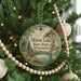 A round ornament hanging on a Christmas tree, featuring a scenic landscape with a lake and mountains.