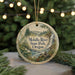 A round ornament with a scenic landscape of the Molalla River State Park in Oregon, featuring a waterfall and pine trees, is displayed on a table with a blurred background of Christmas lights.