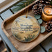 A decorative ornament with a scenic landscape of sand hills and cacti, featuring the text "Monahans Sandhills State Park, Texas" on it, is displayed on a wooden tray alongside pine cones and a lit candle.