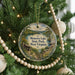 A Christmas tree decorated with ornaments, including a circular ornament with a scenic image of Moncove Lake State Park, West Virginia.